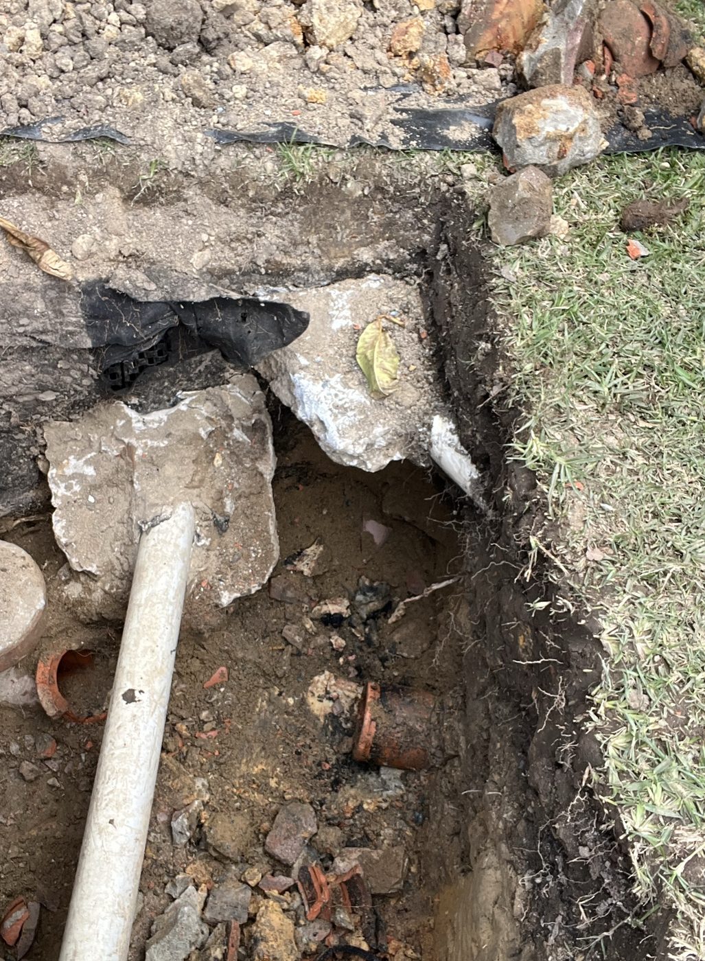 Old clay sewer pipe exposed in a trench beside the lawn in Putney