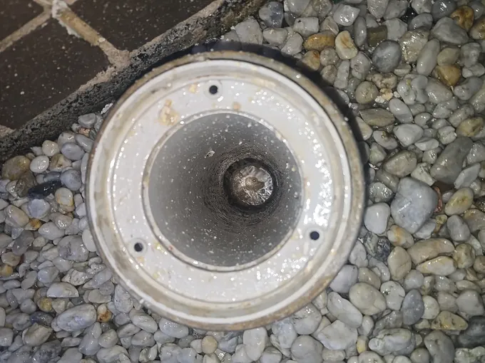 Overflow gully set in pebbles with its grate off and water down inside in The Ponds